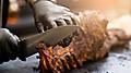 Grill restaurant kitchen. Chef in black cooking gloves using knife to cut smoked pork ribs.